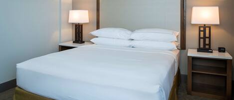 Una cama bien tendida con sábanas blancas, dos mesitas de noche con lámparas y un cabecero de madera.
