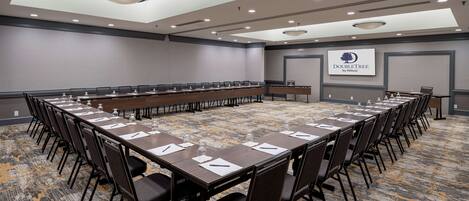 A conference room with a long table, chairs, and a logo on the wall.