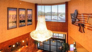 Un hall d’entrée avec un comptoir de réception en marbre, un grand lustre, des tableaux représentant des paysages urbains encadrés, une grande fenêtre offrant une vue panoramique et un élément décoratif mural.