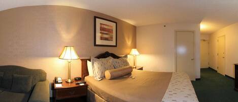 A hotel room with a bed, two bedside lamps, a nightstand, a chair, and a door leading to another room.