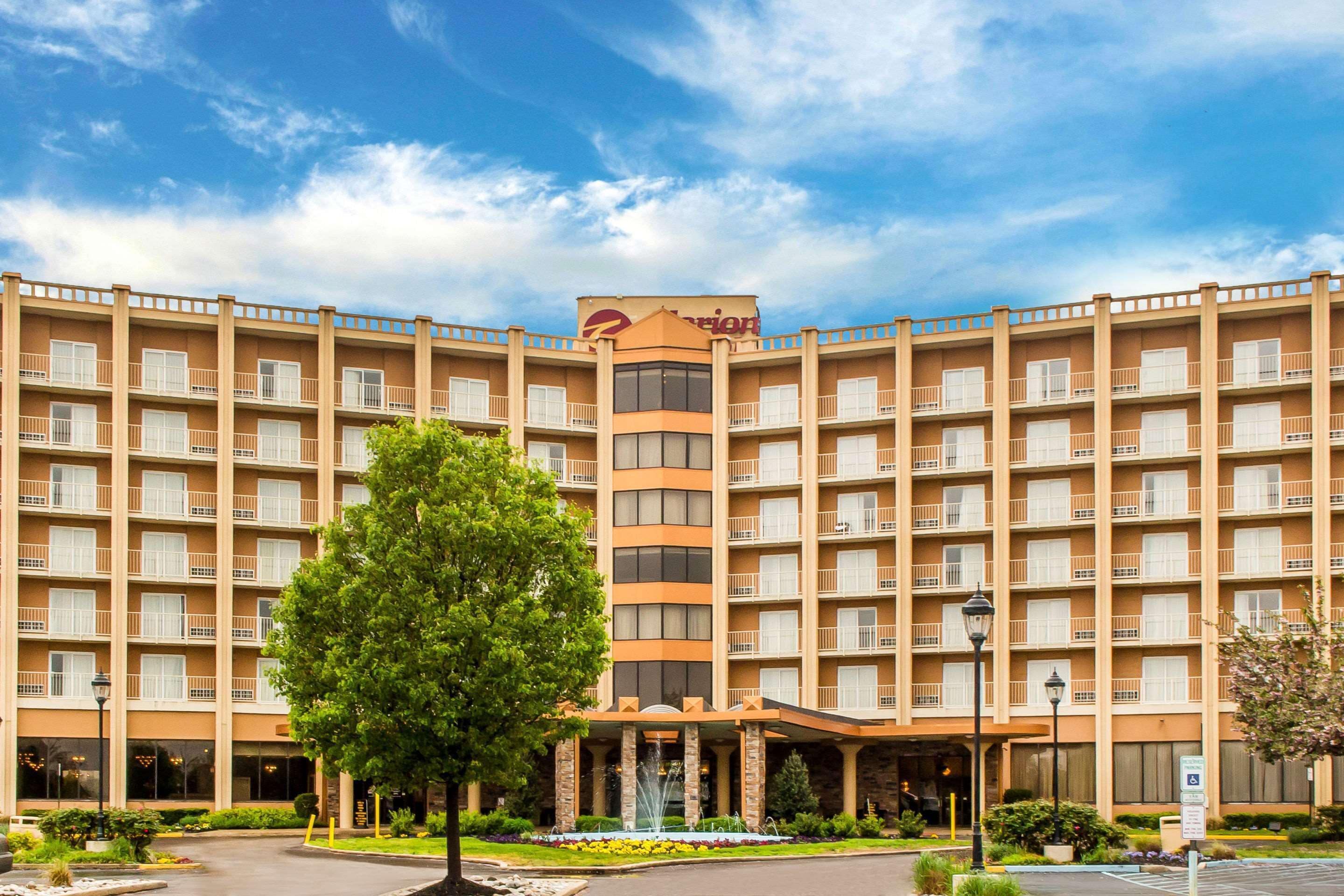 A multi-story hotel with a central entrance, a fountain, and a clear sky.
