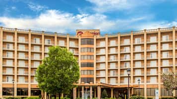 A multi-story hotel with a central entrance, a fountain, and a clear sky.