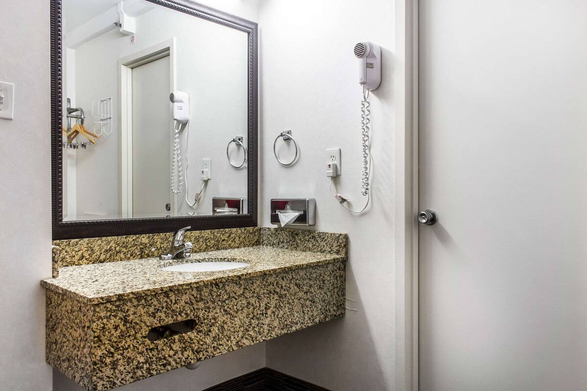 Une salle de bain équipée d’un lavabo avec un plan de travail en granit, d’un miroir, d’un sèche-cheveux et d’un distributeur de serviettes.