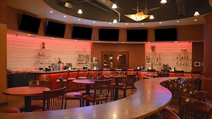Un espace bar offrant différentes options de sièges, notamment des tables rondes et des banquettes, ainsi qu’un comptoir avec des étagères remplies de bouteilles.