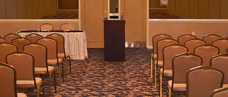 A conference room with rows of chairs facing a podium, carpeted floor, and wooden panel walls.