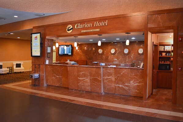 A hotel reception area with a marble counter, clocks, and a digital screen.