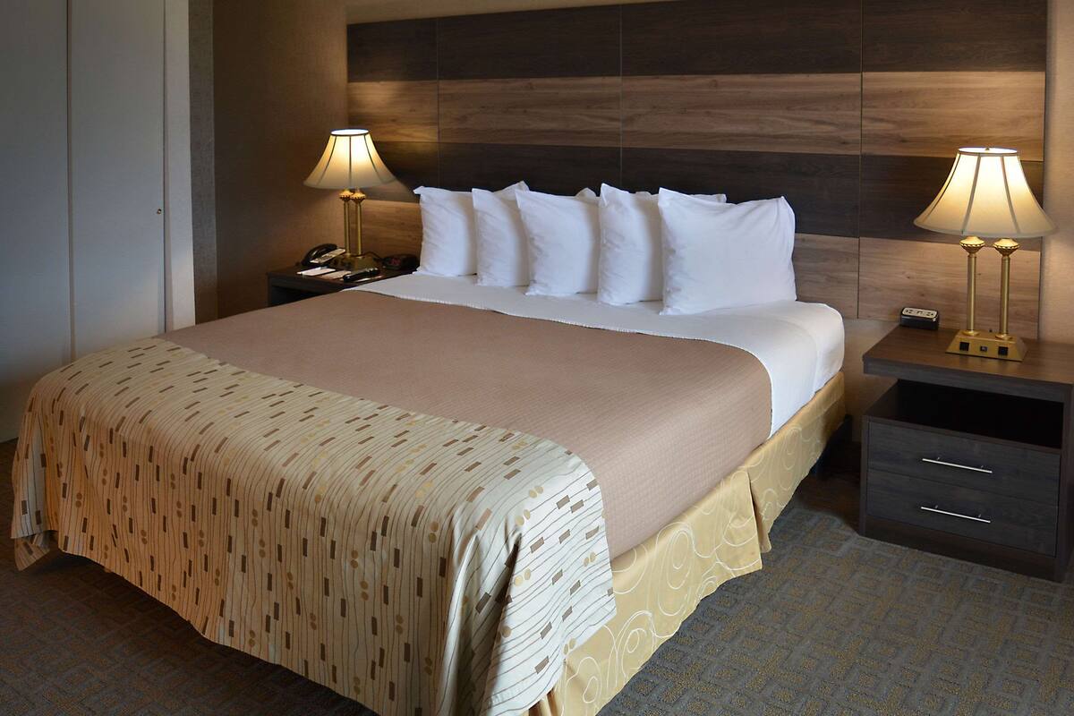 Un lit bien fait, recouvert d’une couvre-lit à motifs, deux tables de chevet avec des lampes et une petite table de nuit avec un téléphone et une télécommande.