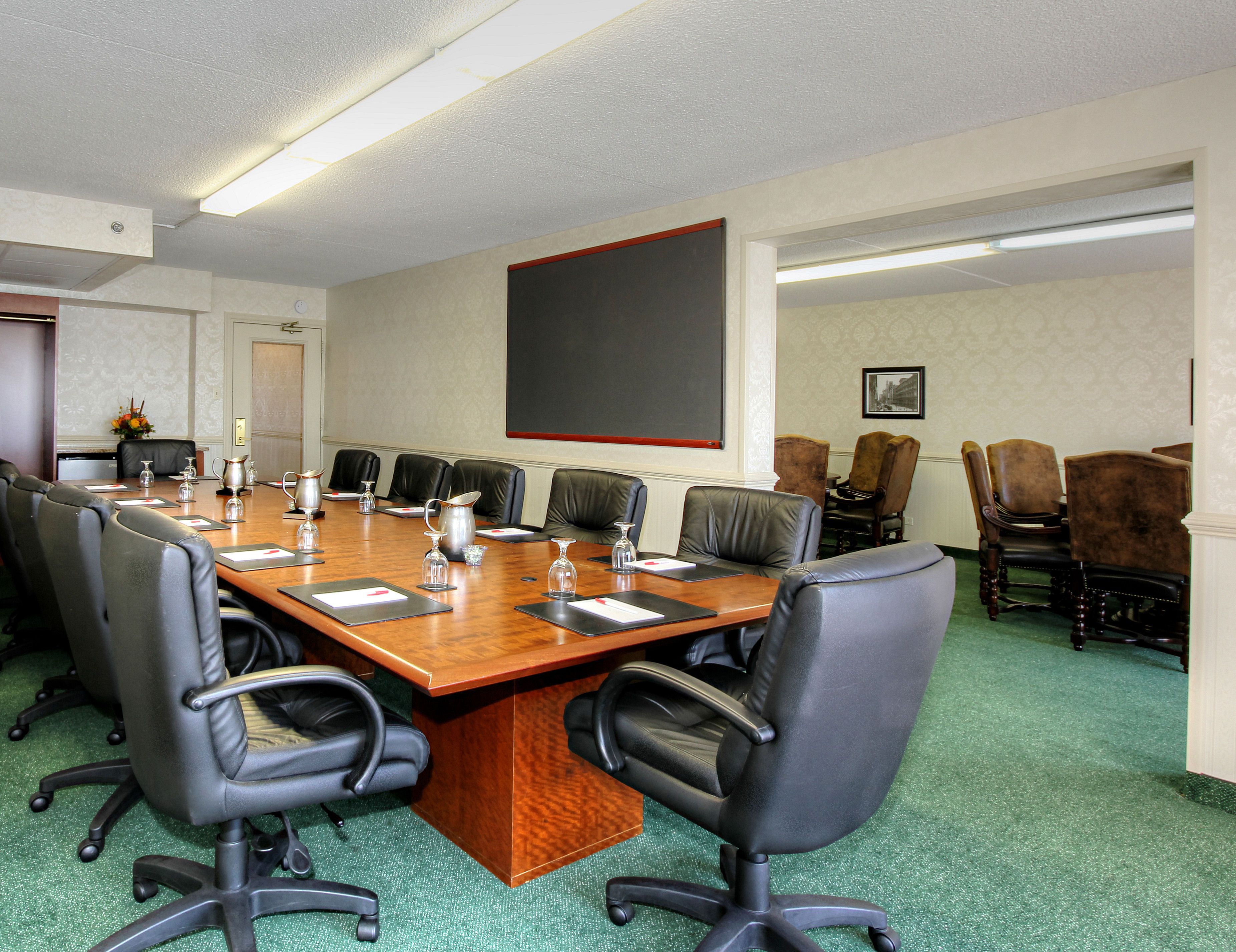 A conference room with a long wooden table, black leather chairs, and a large blackboard on the wall.