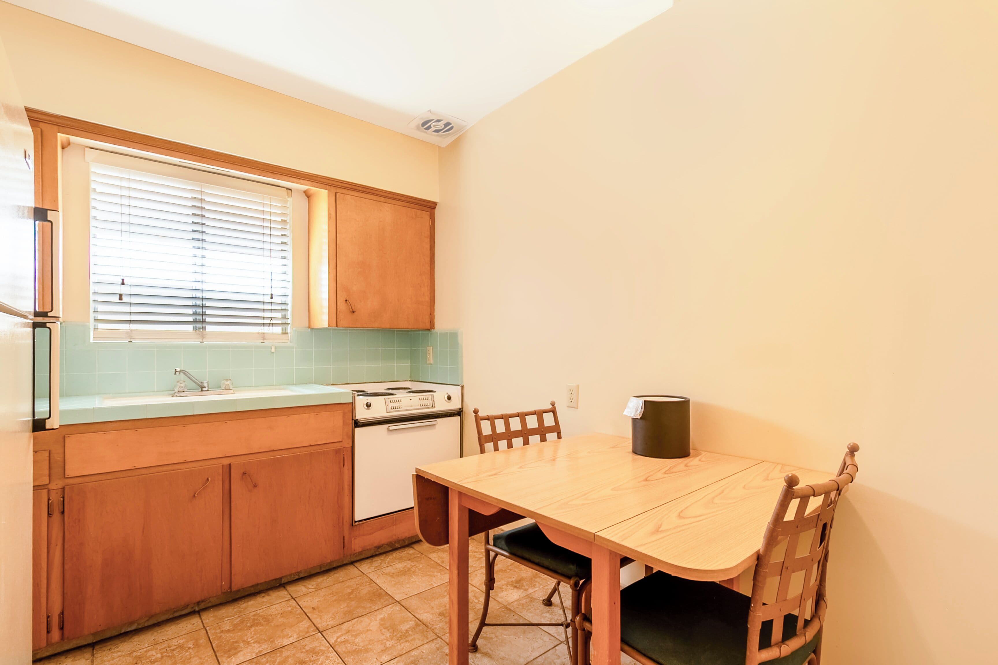 A compact kitchen with a dining table and chairs, a stove, and a window with blinds.