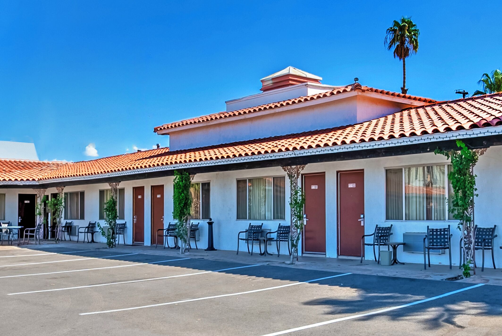 Ein Motel mit einer Reihe von Zimmern, jedes mit Tür und Fenstern, und einem Parkplatz davor.
