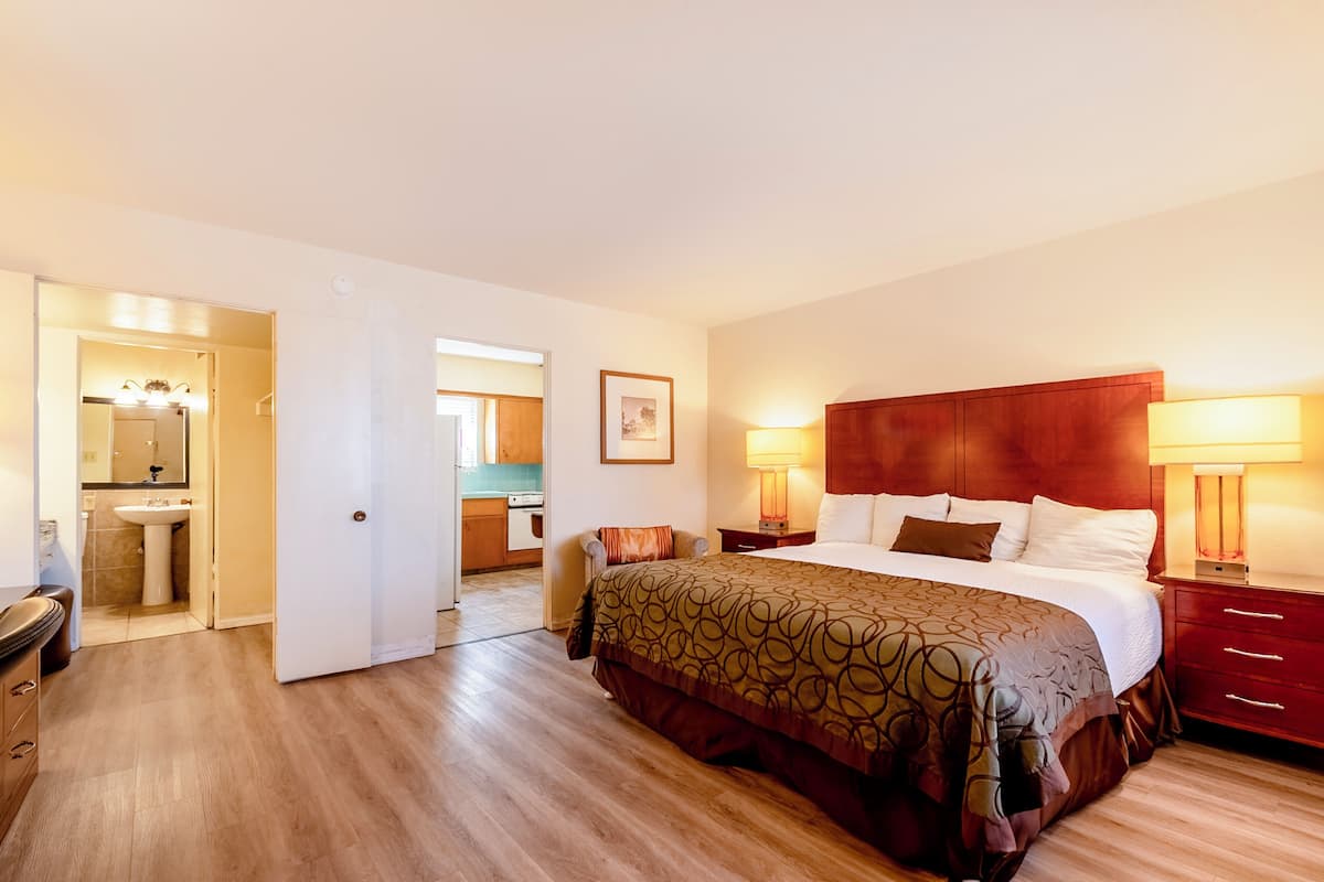 Habitación de hotel con una cama grande, cabecera de madera, lámparas de noche, cómoda de madera y baño visible a través de una puerta abierta.