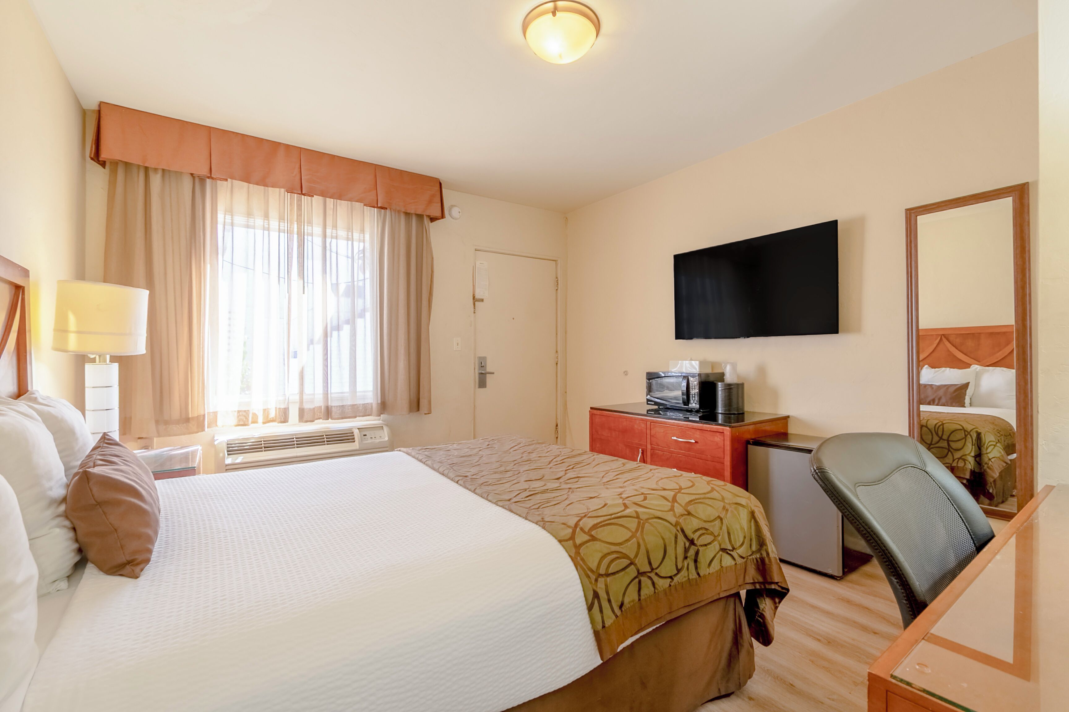 Een hotelkamer met een bed, een bureau met een computer, een televisie en een spiegel.