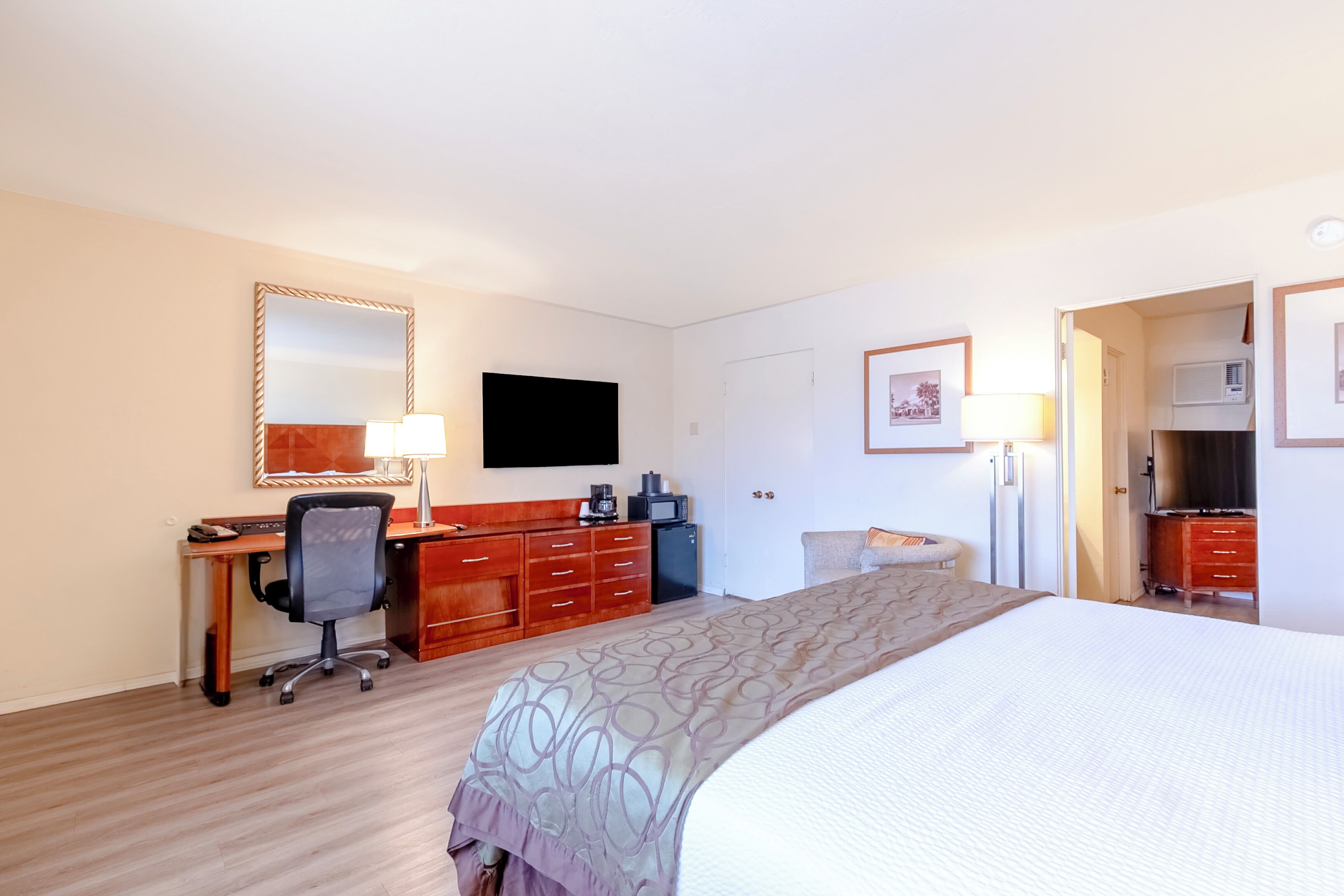 A hotel room with a bed, a desk with a chair, a television, a dresser, and a microwave.