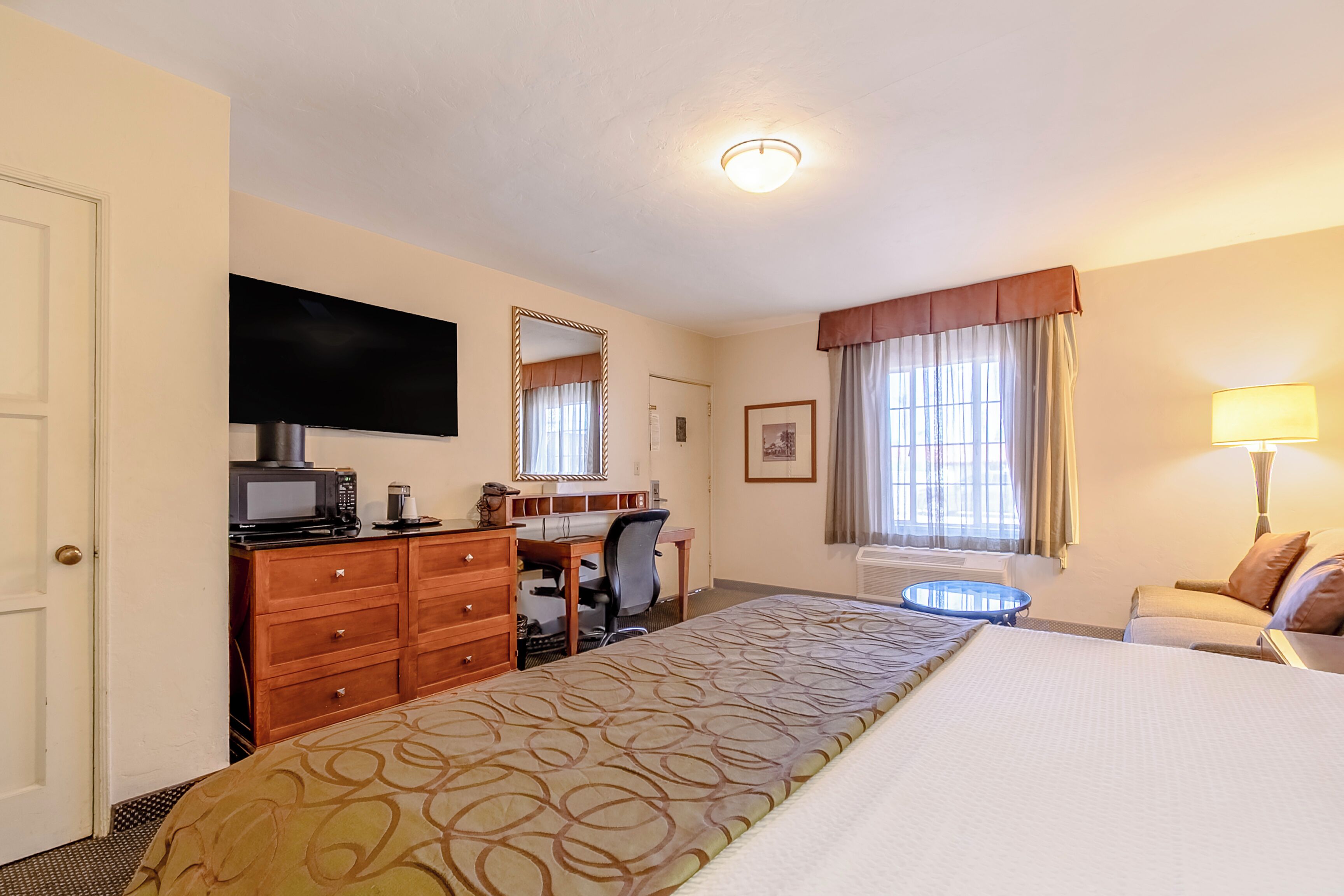 Una habitación de hotel con cama, escritorio, silla, televisor y una mesita.
