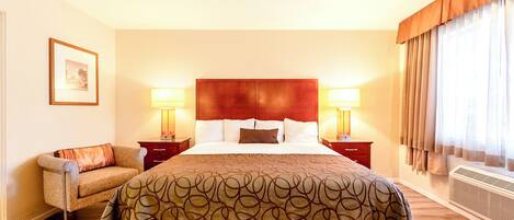 A hotel room with a large bed, two bedside tables with lamps, a chair, and a framed picture on the wall.