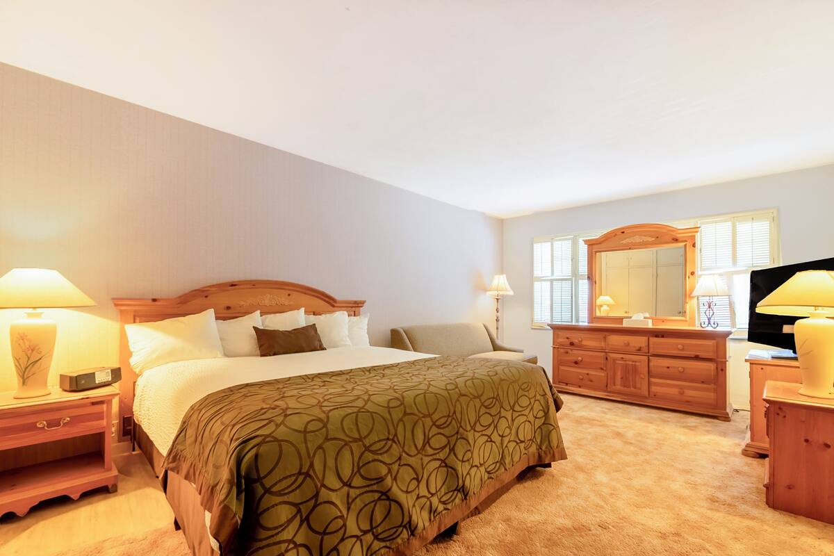 Una habitación de hotel con una cama grande, un aparador de madera, un televisor y dos lámparas de noche.