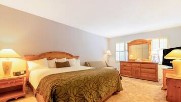 A hotel room with a large bed, a wooden dresser, a television, and two bedside lamps.