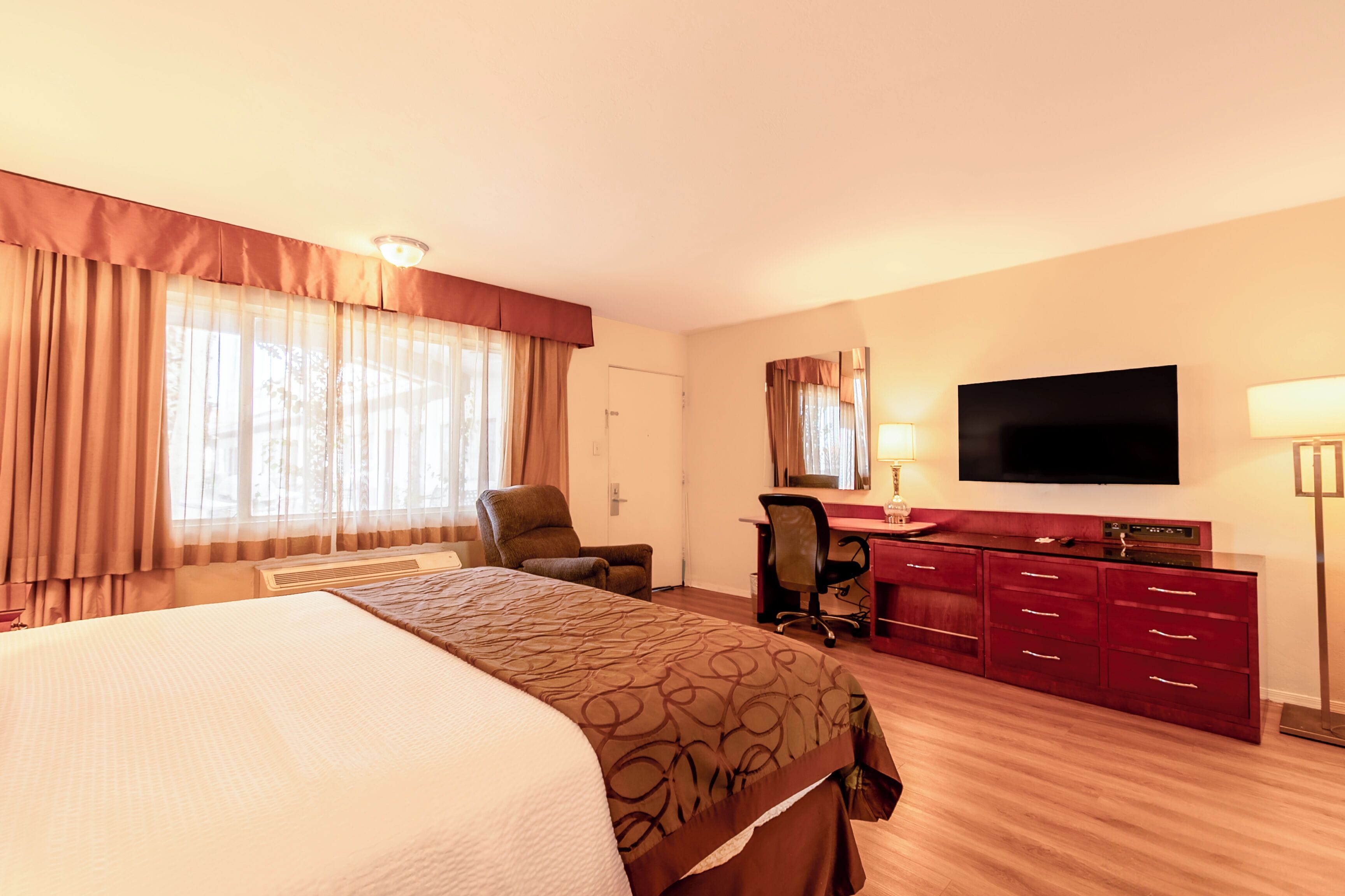 Una habitación de hotel con una cama grande, un escritorio con una silla, un televisor y un aparador.