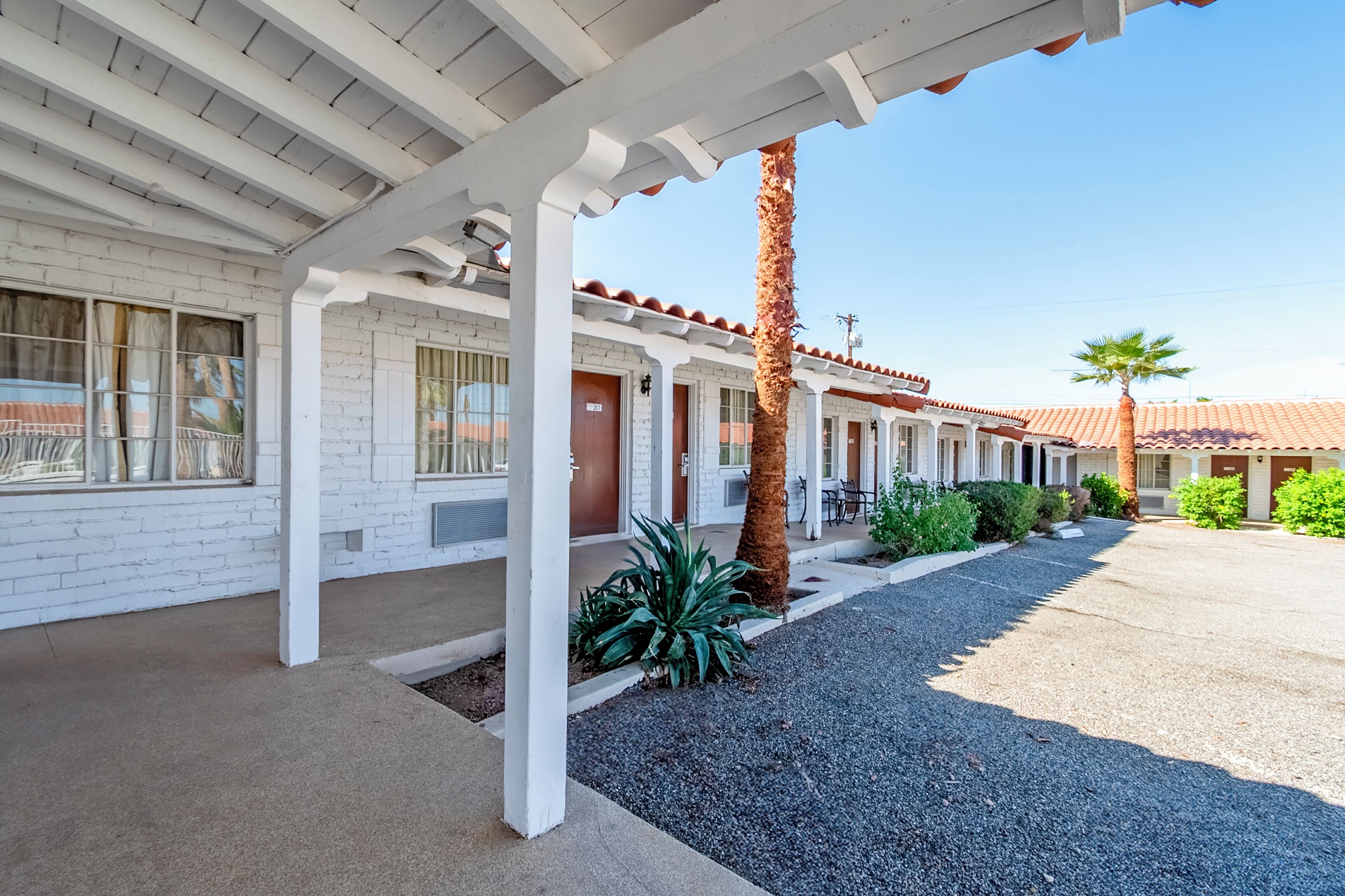 A motel with a white facade, a covered parking area, and a palm tree.