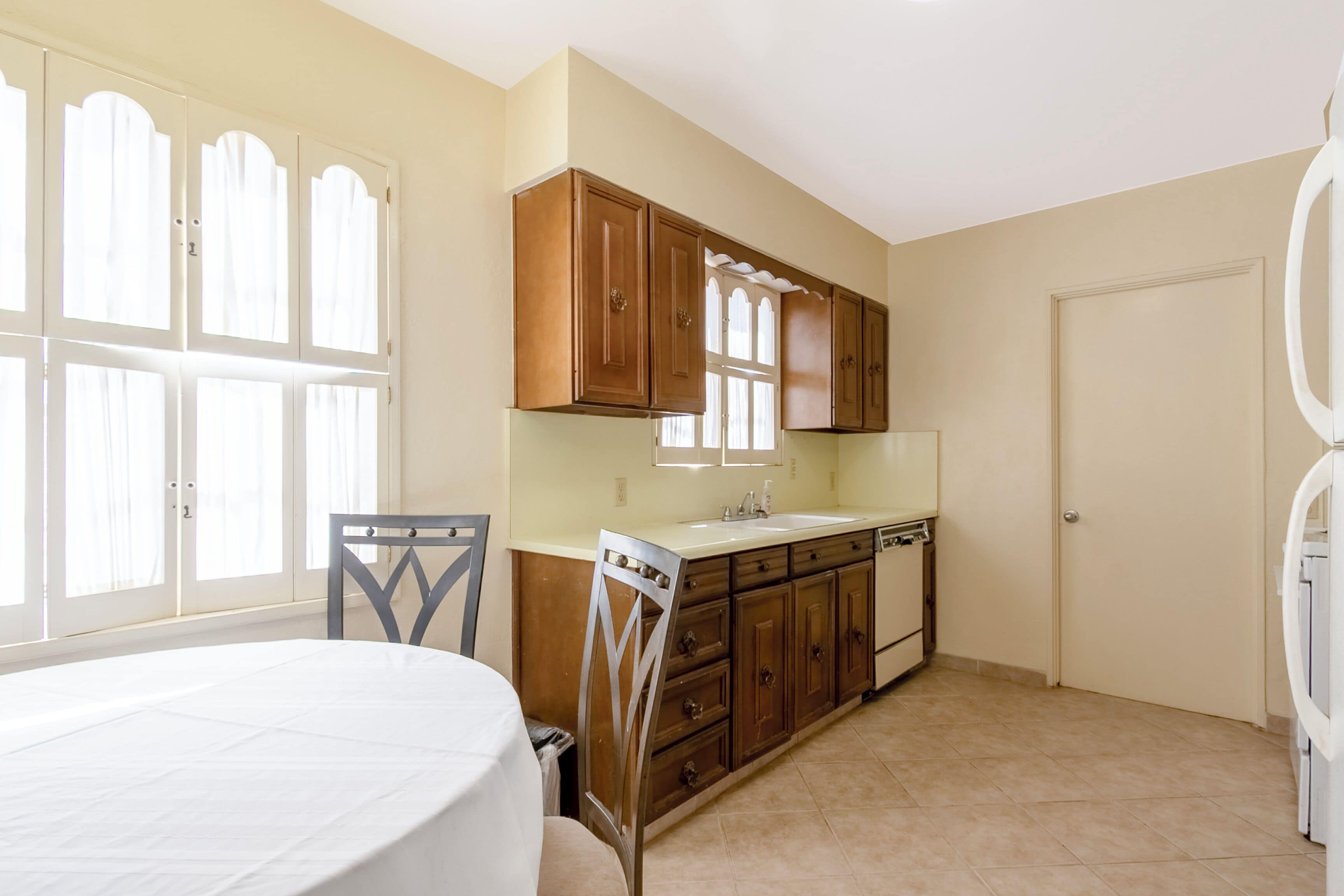 A kitchen with wooden cabinets, a white countertop, and a window with curtains.