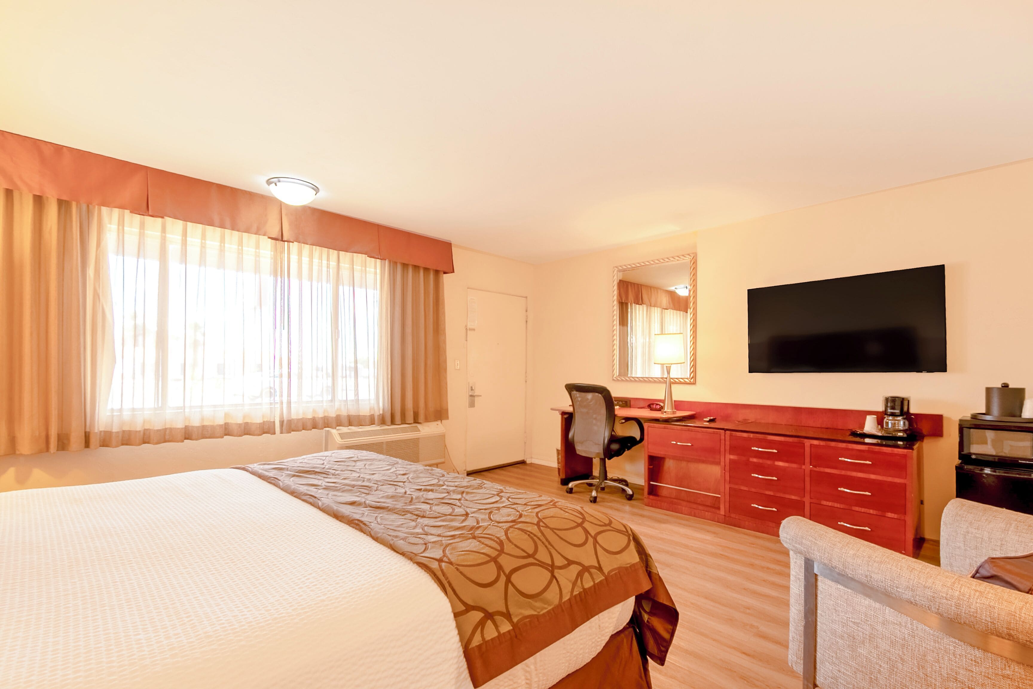 Una habitación de hotel con una cama grande, un escritorio, una silla, un televisor y un aparador rojo.
