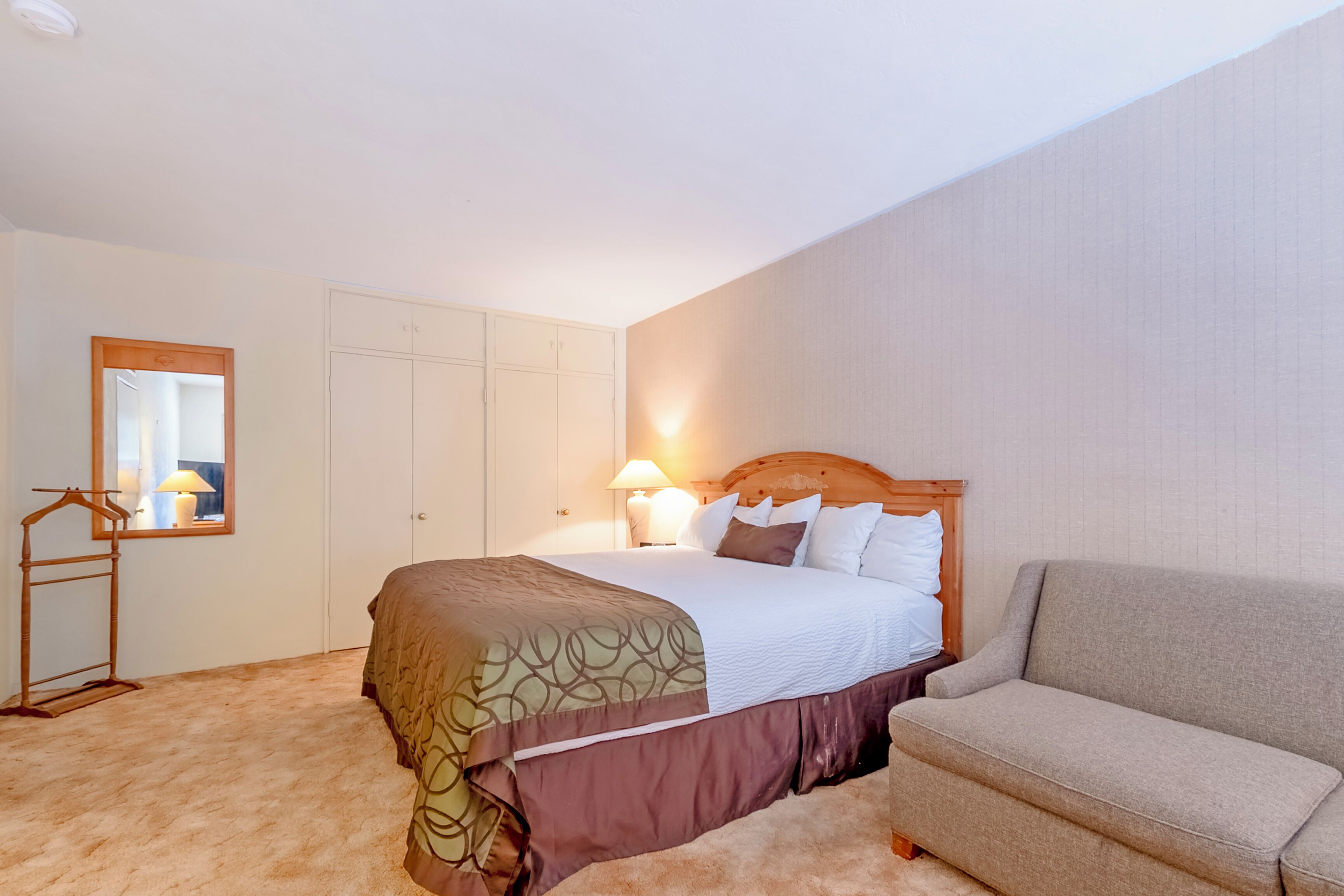 A bedroom with a bed, a bedside table with lamps, a wardrobe, and a sofa.