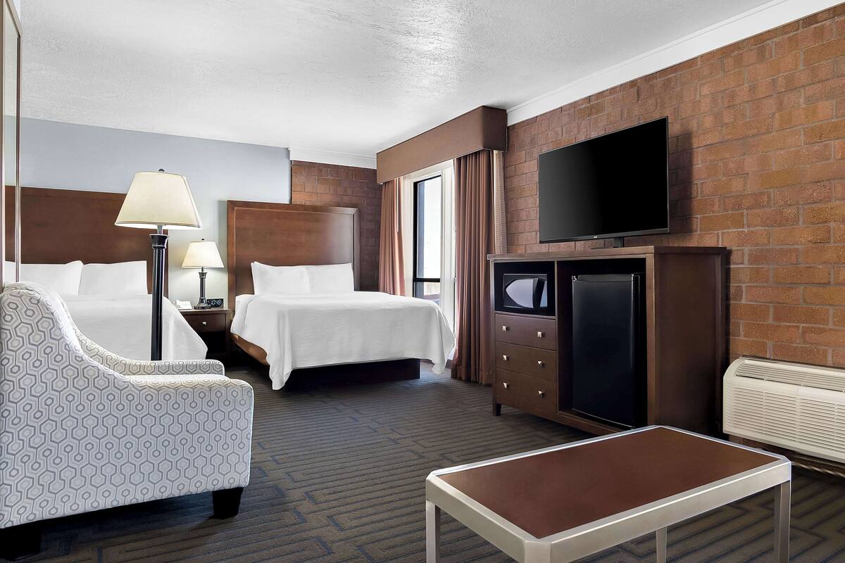 A hotel room with two beds, a TV, a desk, and a chair.