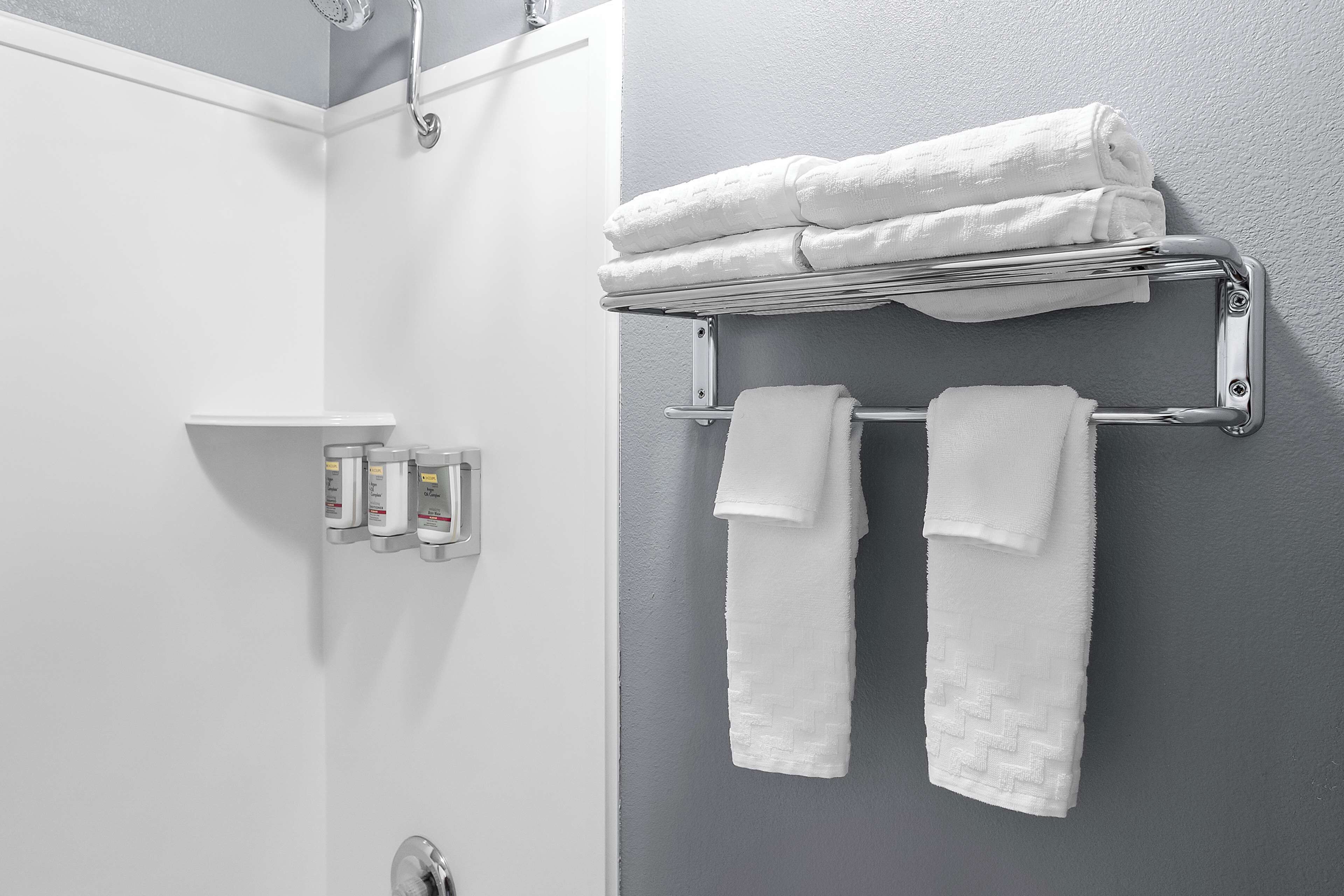 A bathroom with a towel rack holding folded towels, a soap dispenser, and a shower control panel.