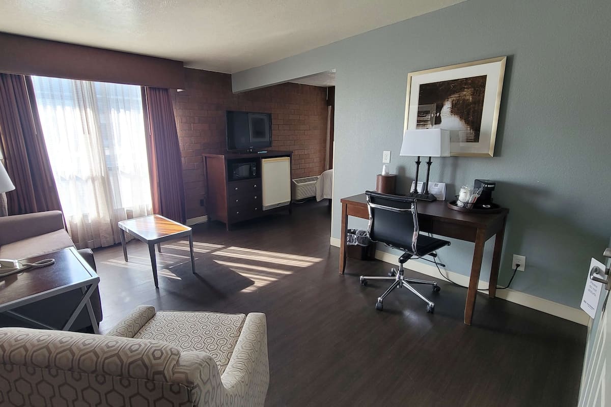 A hotel room with a sofa, a small table, a desk with a chair, a TV, and a picture on the wall.