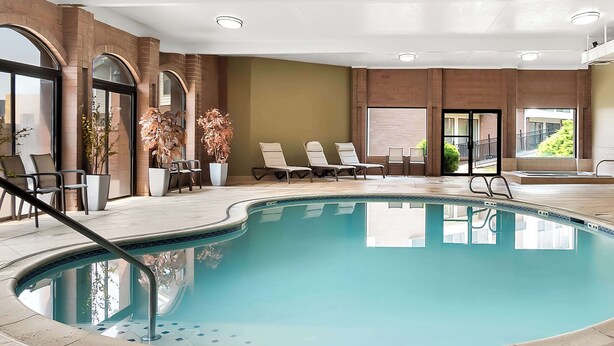 Une piscine intérieure dotée de chaises longues, de plantes en pot et offrant une vue sur l’extérieur.