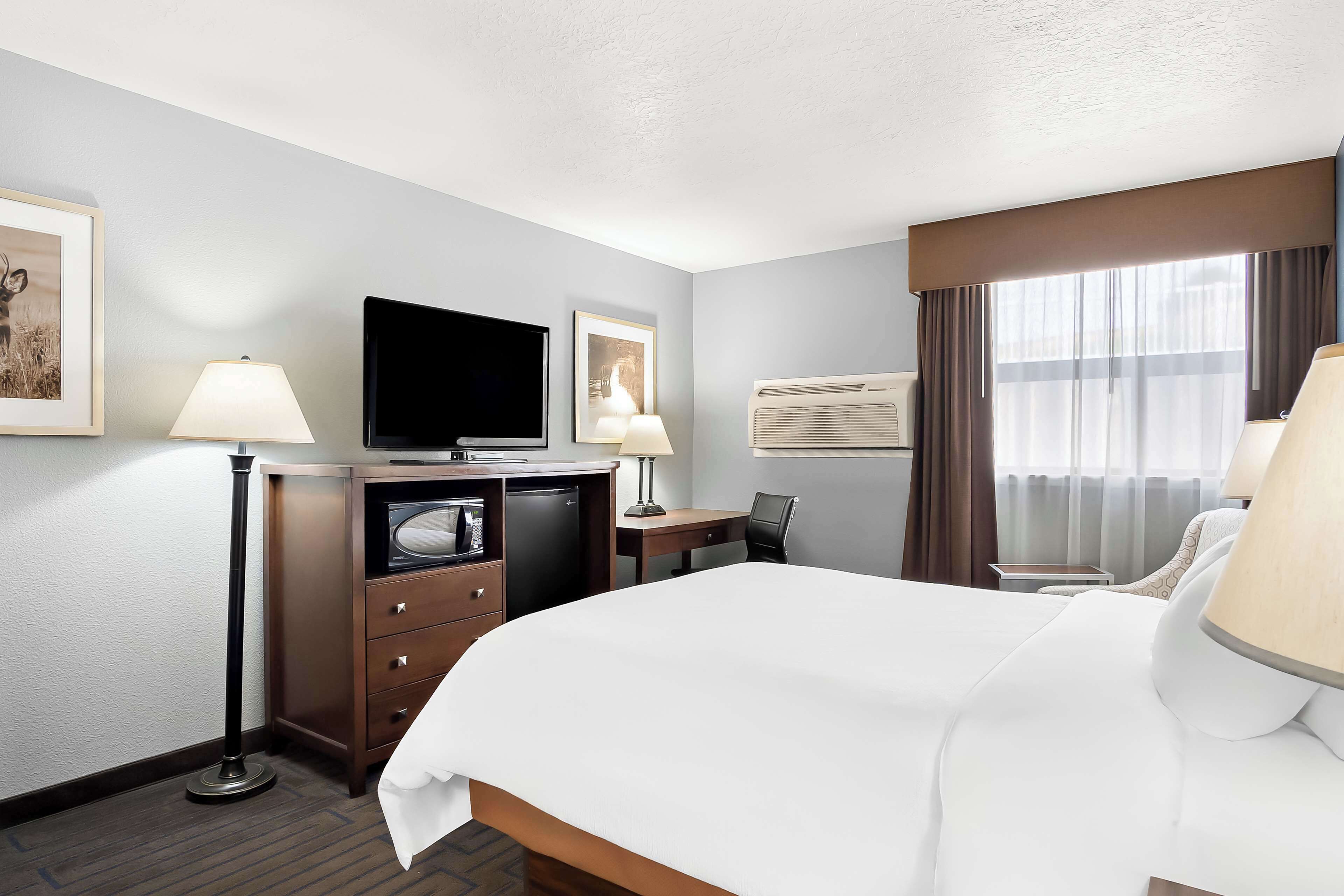 A hotel room with a bed, desk, chair, television, and air conditioning unit.