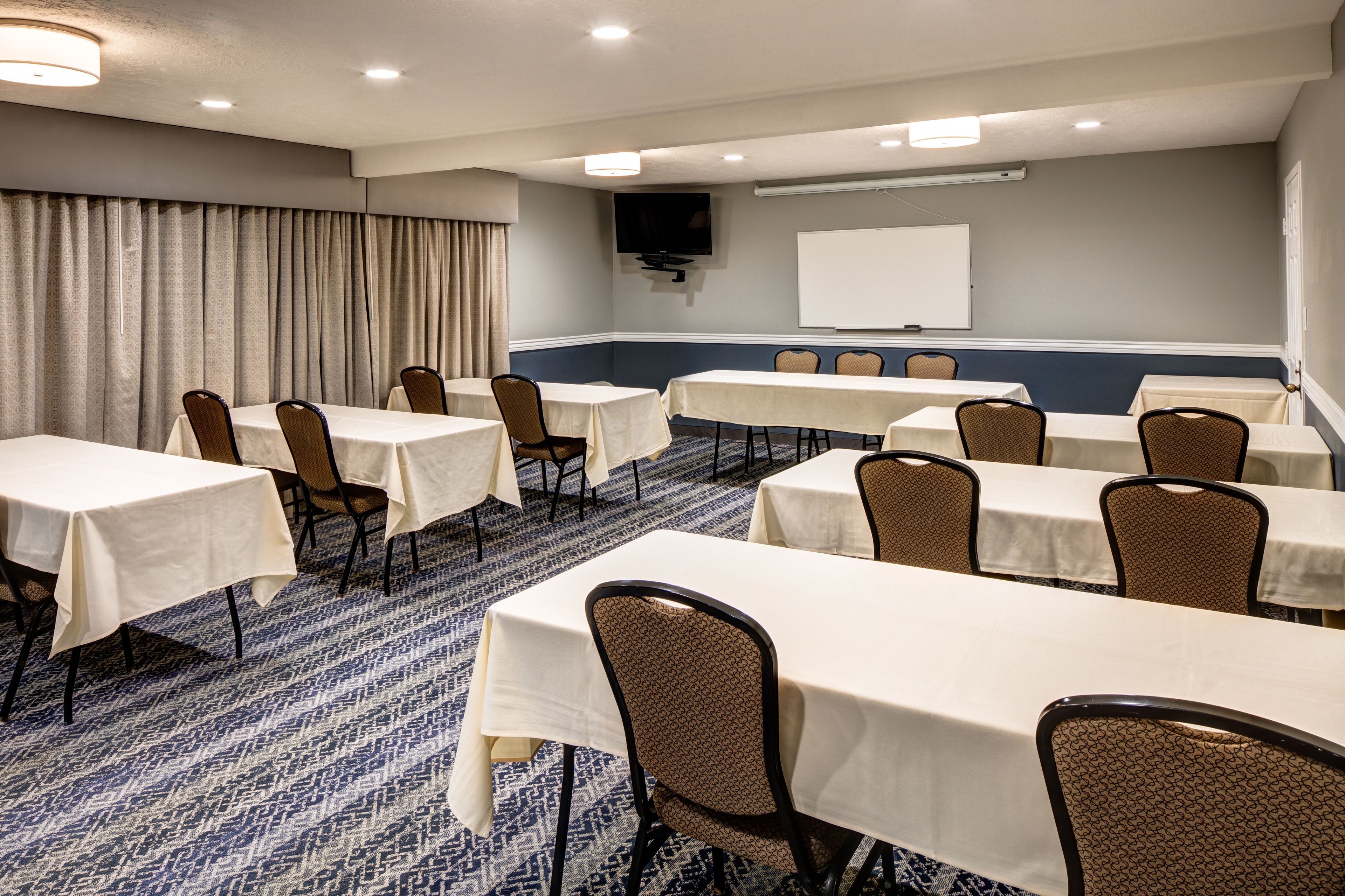 Une salle de conférence équipée de tables et de chaises, d’un tableau blanc et d’un téléviseur fixé au mur.