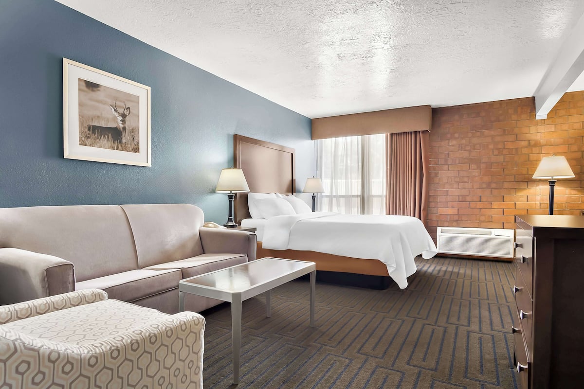 A hotel room with a bed, a sofa, a coffee table, a desk, and a lamp.