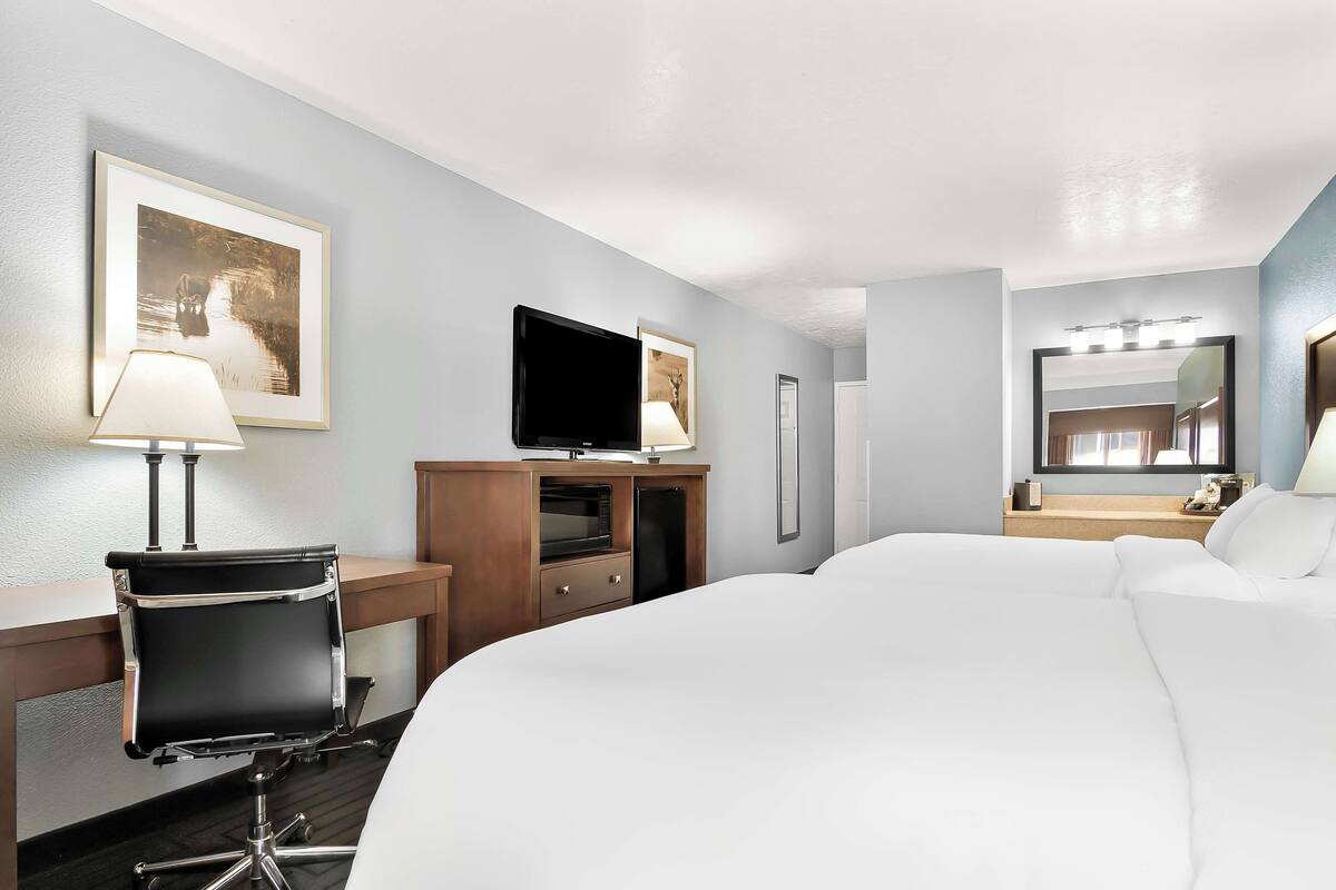A hotel room with a large bed, a desk with a lamp, a television, and a mirror.