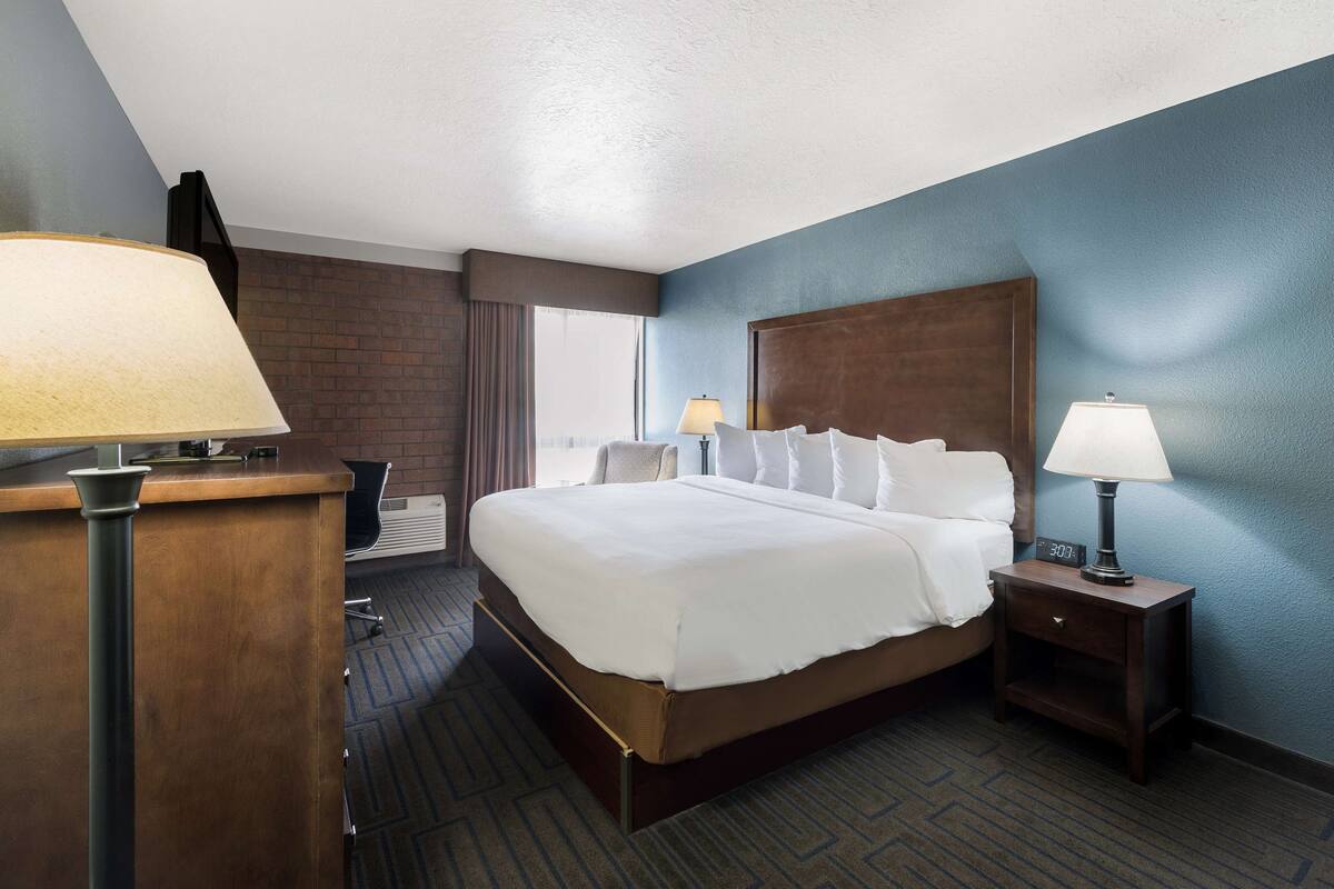 A hotel room with a large bed, two bedside tables with lamps, a desk, and a chair.