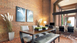 Un hall d’hôtel moderne avec un mur en briques, deux œuvres d’art, un espace repas avec une table et des chaises, et un banc.