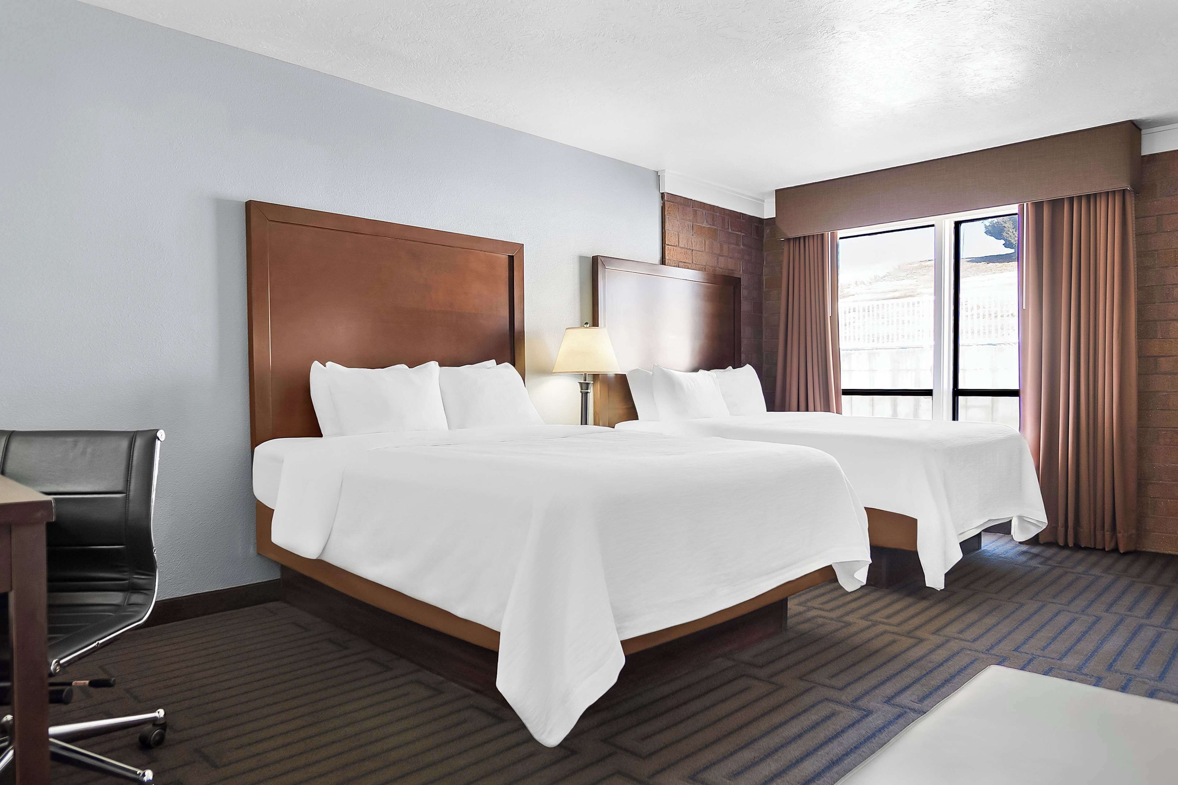 A hotel room with two beds, a desk, and a chair.