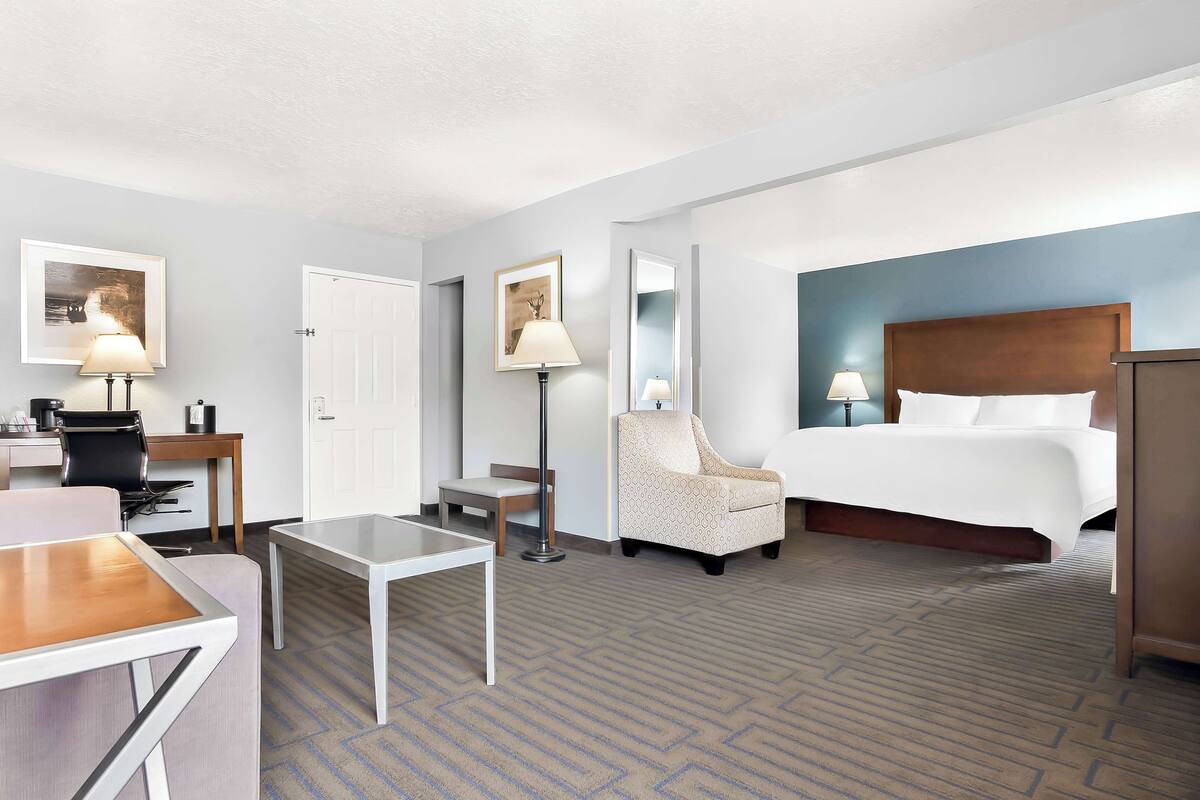 A hotel room with a bed, a desk, a chair, a table, and two lamps.