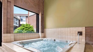 Un bain à remous dans une pièce aux murs carrelés, avec une fenêtre donnant sur un bâtiment en briques.