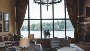 Amplia sala de estar con un gran ventanal con vista a un lago, amoblada con sofás y lámparas.