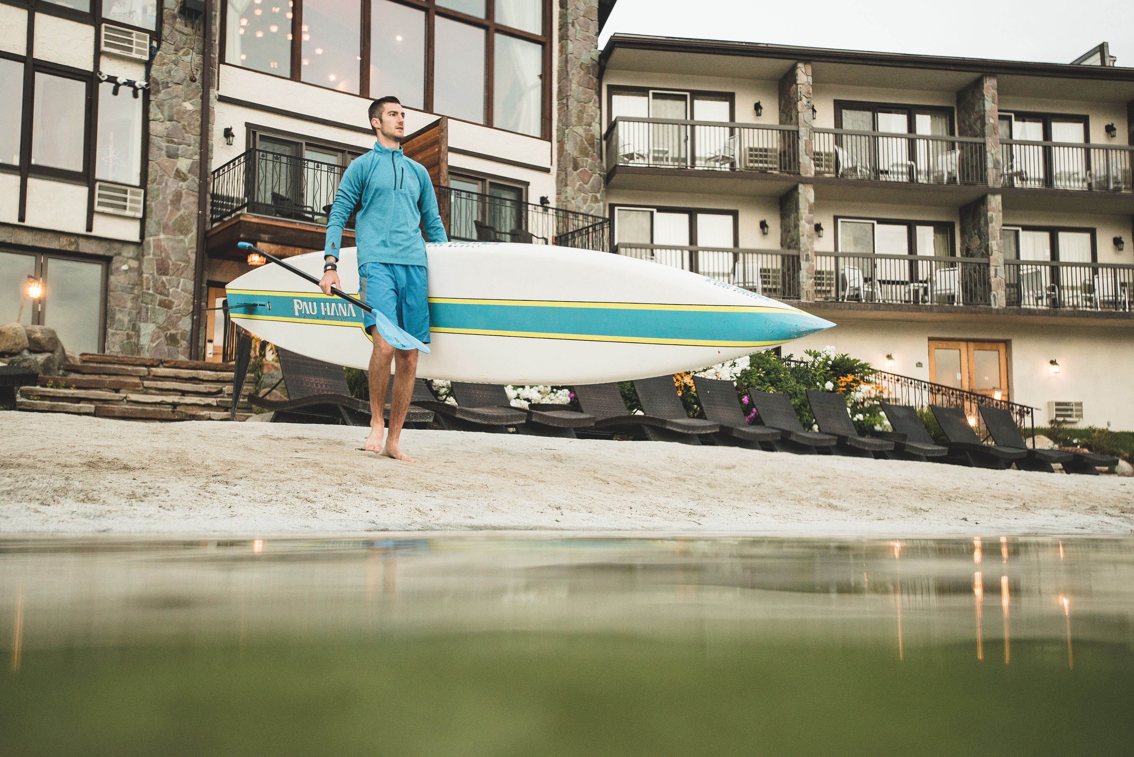 A person standing next to a surfboard in front of a building with multiple balconies and a pool.