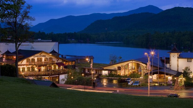 Un hotel con vista al lago, una torre de reloj y montañas al fondo.
