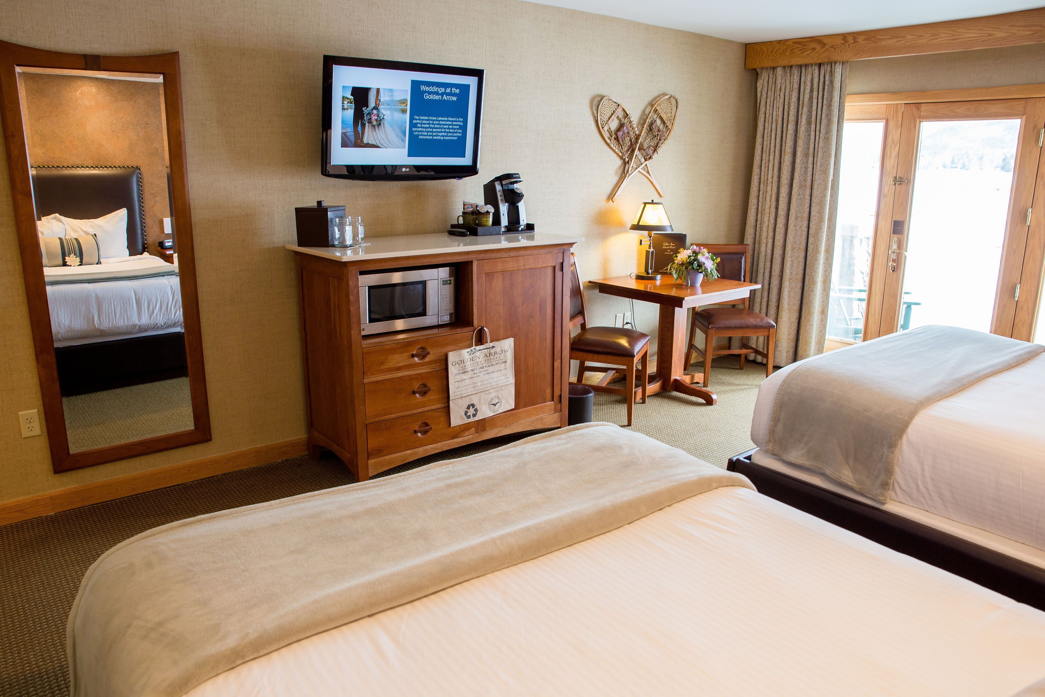 A hotel room with a bed, a desk with a computer, a television, and a view of the outdoors.