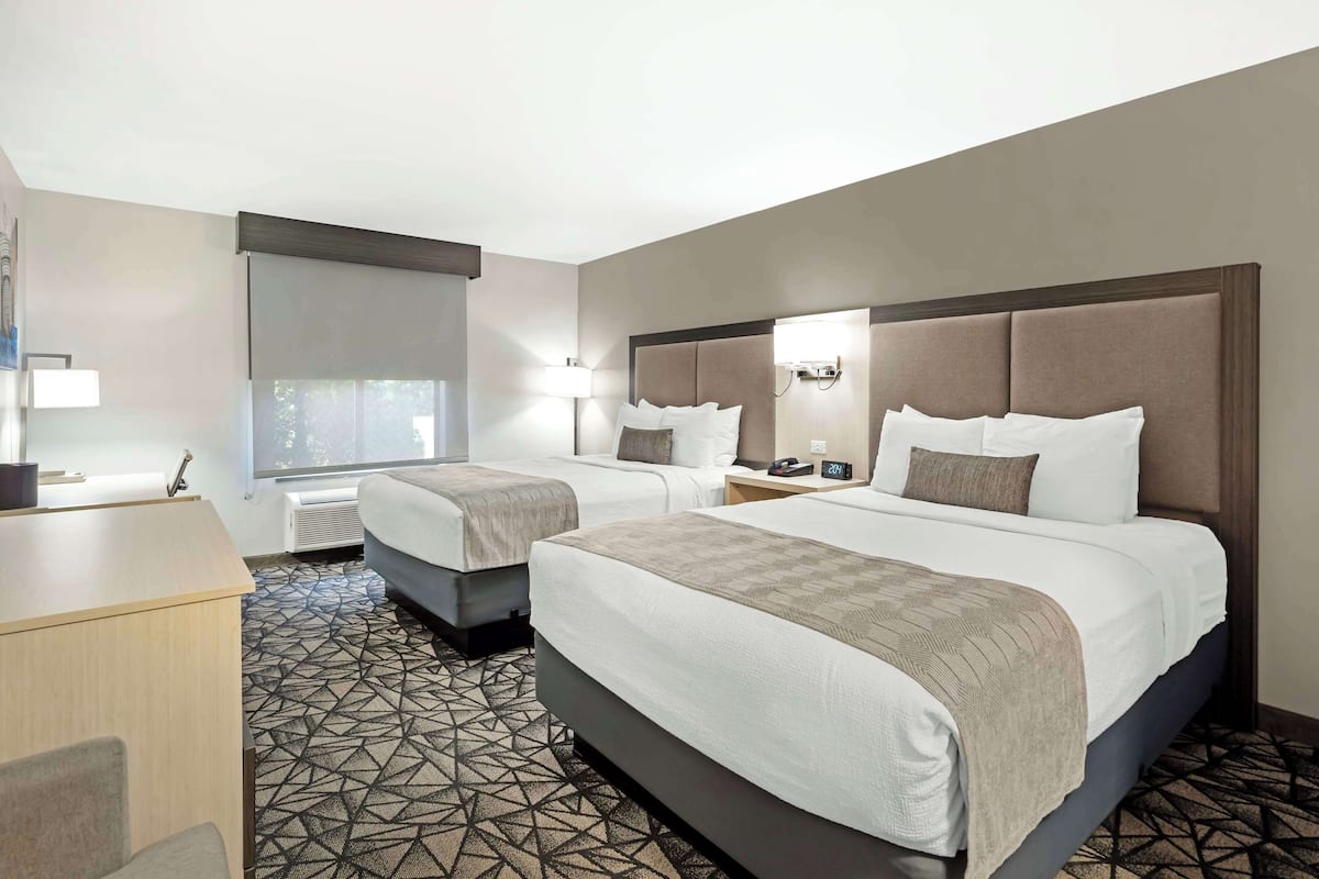 A hotel room with two beds, a desk, and a patterned carpet.