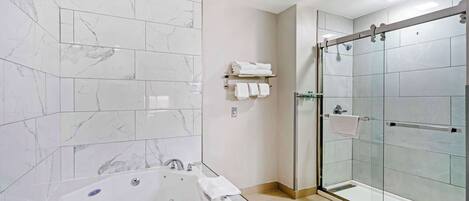 A bathroom with a large bathtub, a glass-enclosed shower, and marble tiles.