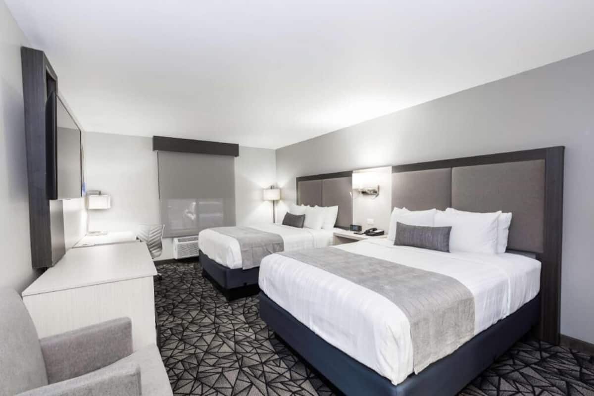 A hotel room with two beds, a desk, a chair, a large mirror, and a patterned carpet.