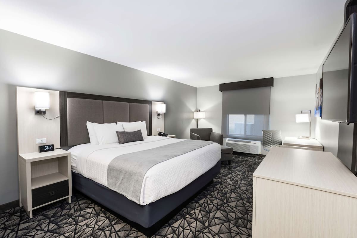 A hotel room with a bed, bedside tables, a desk, a chair, a TV, and a window.