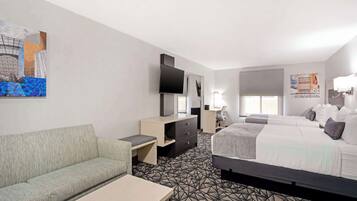 Una habitación de hotel con sofá, cama, escritorio, cómoda, televisor y obras de arte en las paredes.