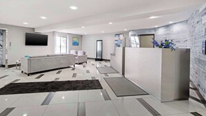 A modern hotel lobby with a reception desk, sofas, and a large flat-screen TV.
