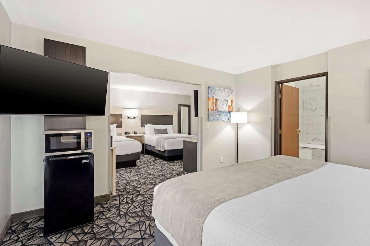 A hotel room with a bed, a flat-screen TV, a microwave, a refrigerator, and a bathroom visible through an open door.